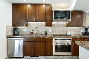 Kitchen featuring dark brown cabinetry, appliances with stainless steel finishes, a sink, backsplash, and recessed lighting