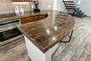 Kitchen featuring wood finish floors, backsplash, stainless steel oven, and brown cabinets