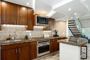 Kitchen with a breakfast bar area, backsplash, appliances with stainless steel finishes, a sink, and a peninsula