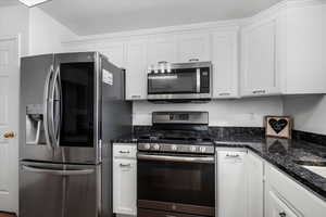 Kitchen with dark stone counters, white cabinetry, and stainless steel appliances