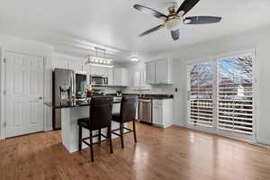 Kitchen featuring ceiling fan, a center island, a kitchen bar, white cabinets, and appliances with stainless steel finishes