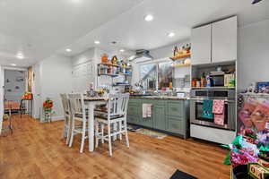 Kitchen with white cabinetry, oven, green cabinets, and light hardwood / wood-style flooring