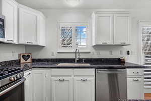 Kitchen with white cabinets, appliances with stainless steel finishes, dark stone counters, and sink