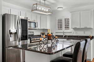 Kitchen featuring white cabinetry, sink, hanging light fixtures, stainless steel appliances, and dark stone countertops