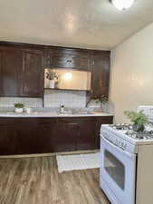 Unit #2 - Kitchen featuring light wood-type flooring, decorative backsplash, white gas range oven, and sink