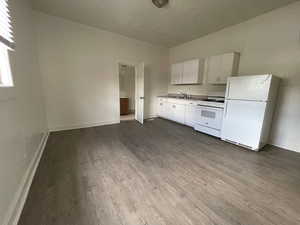 Unit #1 - Kitchen featuring sink, white cabinets, dark wood-type flooring, and white appliances