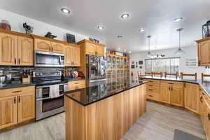 Kitchen with hanging light fixtures, an inviting chandelier, tasteful backsplash, light hardwood / wood-style flooring, and appliances with stainless steel finishes