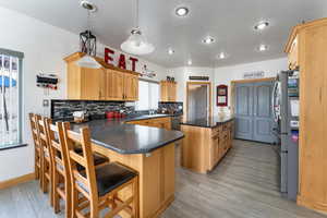 Kitchen featuring hanging light fixtures, a kitchen breakfast bar, tasteful backsplash, appliances with stainless steel finishes, and light wood-type flooring