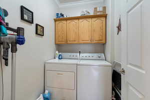 Clothes washing area featuring cabinets, washing machine and dryer, and ornamental molding