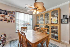 Tiled dining room with ceiling fan and crown molding