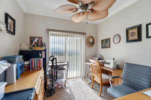 Carpeted office space with ceiling fan and crown molding