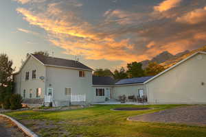 Back house at dusk with a lawn, a patio area, and a jacuzzi