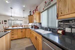 Kitchen with stainless steel dishwasher, sink, backsplash, and an inviting chandelier