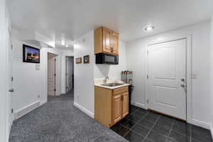 Kitchen with light brown cabinets, dark carpet, and sink