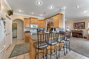 Kitchen featuring kitchen peninsula, washer / clothes dryer, crown molding, white appliances, and a kitchen bar