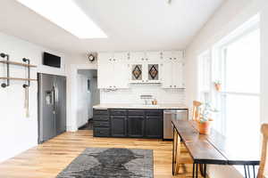 Kitchen with white cabinets, sink, appliances with stainless steel finishes, tasteful backsplash, and light hardwood / wood-style floors