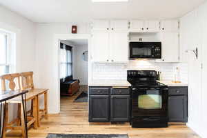 Kitchen featuring light wood-type flooring, tasteful backsplash, white cabinetry, and black appliances