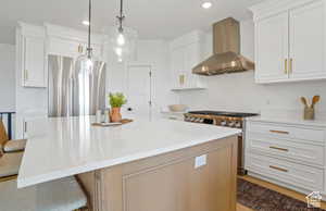 Kitchen featuring white cabinets, stainless steel appliances, wall chimney exhaust hood, and a spacious island