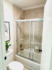 Bathroom with toilet and bath / shower combo with glass door