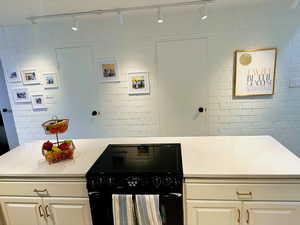 Kitchen featuring white cabinetry, black range oven, brick wall, and track lighting