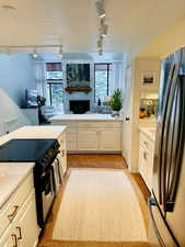 Kitchen with rail lighting, white cabinets, stainless steel refrigerator, black / electric stove, and a stone fireplace