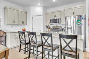 Kitchen with appliances with stainless steel finishes, light stone counters, light hardwood / wood-style flooring, gray cabinets, and a breakfast bar area