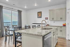 Kitchen with light stone countertops, tasteful backsplash, stainless steel dishwasher, a kitchen island with sink, and sink