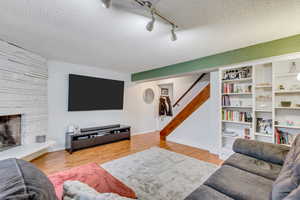 Living room featuring a fireplace, light hardwood / wood-style flooring, a textured ceiling, and track lighting