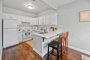 Kitchen featuring sink, kitchen peninsula, white appliances, a breakfast bar, and white cabinets