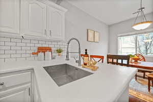 Kitchen featuring white cabinets, sink, hanging light fixtures, and tasteful backsplash