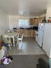 Kitchen with sink, a textured ceiling, white appliances, and light tile patterned flooring