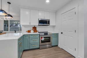 Kitchen with hanging light fixtures, kitchen peninsula, light hardwood / wood-style floors, white cabinets, and appliances with stainless steel finishes