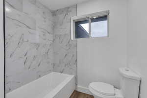 Bathroom with toilet, tiled shower / bath combo, and hardwood / wood-style flooring