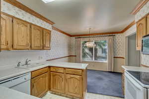 Kitchen with sink, a notable chandelier, crown molding, pendant lighting, and white appliances