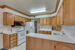 Kitchen with sink, kitchen peninsula, washer / clothes dryer, white appliances, and ornamental molding