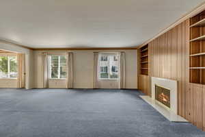 Unfurnished living room featuring carpet, plenty of natural light, and crown molding