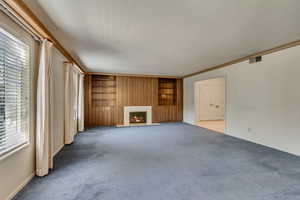 Unfurnished living room featuring built in shelves, light carpet, crown molding, and a healthy amount of sunlight