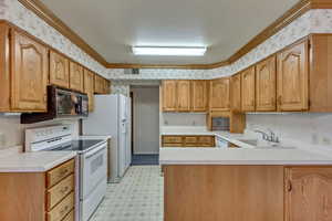 Kitchen with kitchen peninsula, white appliances, crown molding, and sink