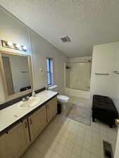 Full bathroom with tile patterned floors, vanity, tiled shower / bath combo, a textured ceiling, and toilet