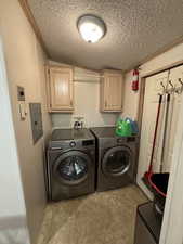 Laundry area with a textured ceiling, cabinets, separate washer and dryer, and crown molding