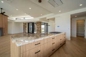 Kitchen featuring light stone countertops, light brown cabinetry, light wood-type flooring, stainless steel gas cooktop, and a large island