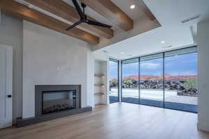 Unfurnished living room featuring floor to ceiling windows, ceiling fan, beamed ceiling, a mountain view, and light hardwood / wood-style floors