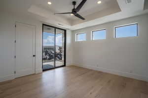 Unfurnished room featuring a raised ceiling, ceiling fan, and light wood-type flooring