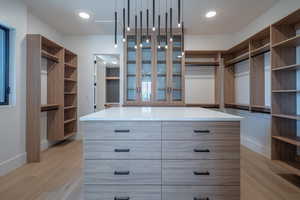 Walk in closet with light hardwood / wood-style flooring