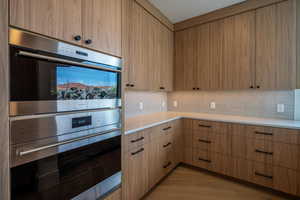 Kitchen with decorative backsplash, stainless steel double oven, and light brown cabinetry