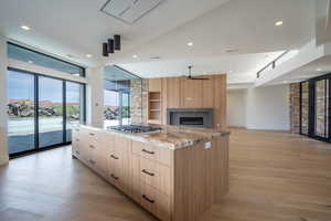 Kitchen featuring stainless steel gas stovetop, ceiling fan, light stone countertops, light brown cabinetry, and a large island