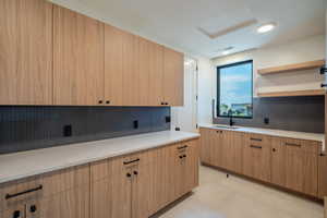 Kitchen featuring light brown cabinets, backsplash, light stone counters, and sink