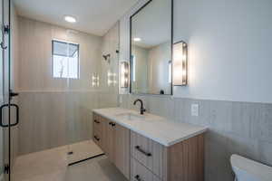 Bathroom with walk in shower, vanity, tile walls, and toilet