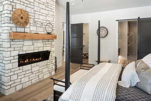 Bedroom with wood-type flooring, a barn door, a stone fireplace, and lofted ceiling