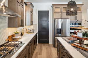 Kitchen featuring exhaust hood, sink, hanging light fixtures, light hardwood / wood-style flooring, and stainless steel appliances